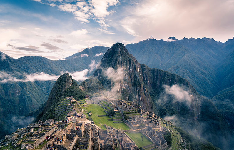 macchu pichu seen on a sunny day with clouds surrounding the mountains