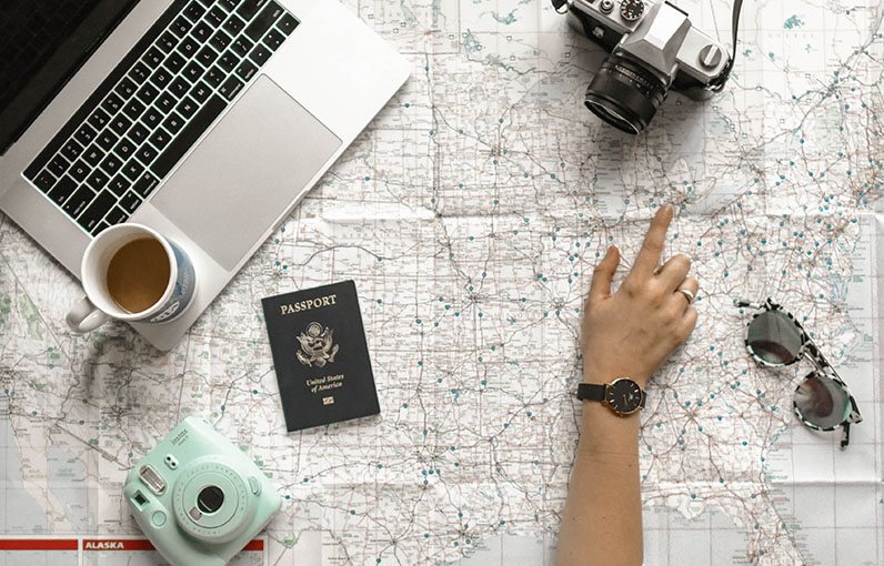 still life of a map, laptop, passport, sunglasses, camera and cup of coffee