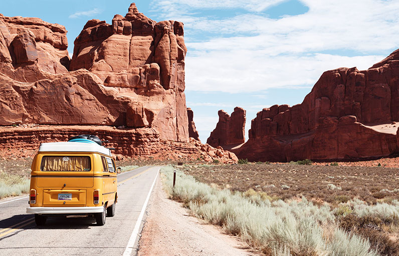 yellow camper van driving through a desert landscape
