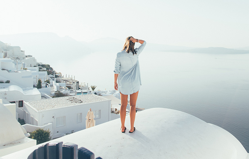 woman wearing a white shirt standing on a rooftop overlooking buildings and the sea